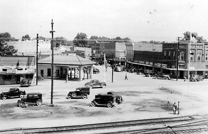 Busy streets and gas station with buildings in the background and railroad tracks in the foreground