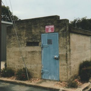 Small concrete building with blue metal door under red sign and tiny windows