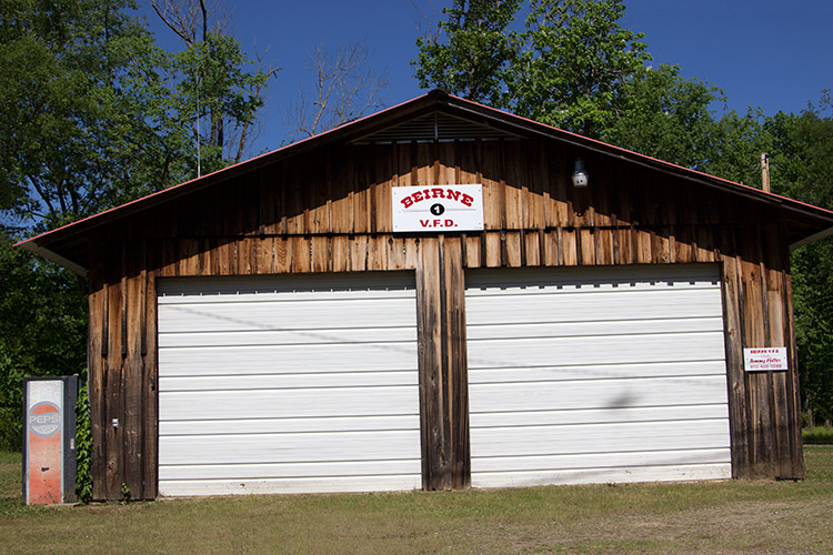 Two-bay garage building with wood siding and sign