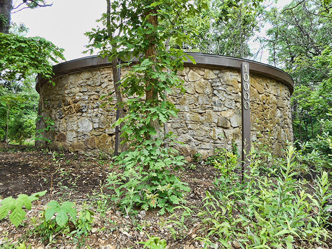 Exterior of large round water tank with stone wall surrounded by trees