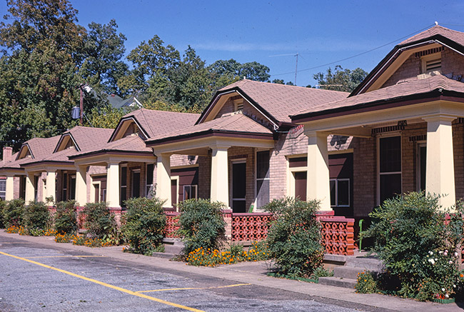 Single-story housing units with gabled roofs and covered porches on parking lot