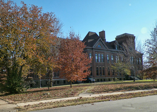 multistory brick building with tower and rows of windows and autumn trees in front