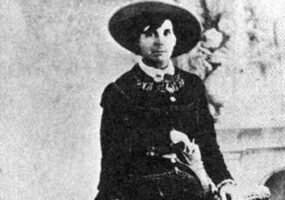 Old white woman in hat and dress holding a revolver
