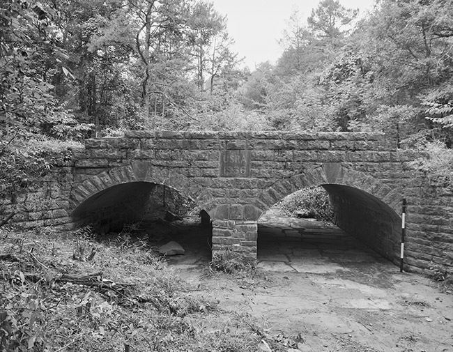 Side view of stone bridge with two arches in forested area