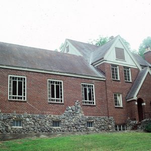 Multistory brick and stone house with stone chimney large windows and a green lawn