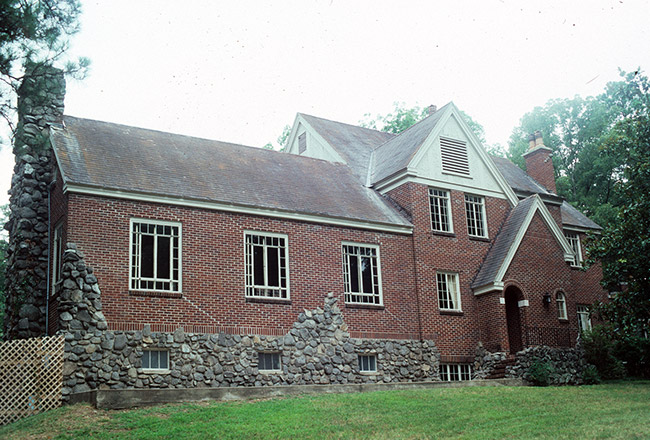 Multistory brick and stone house with stone chimney large windows and a green lawn