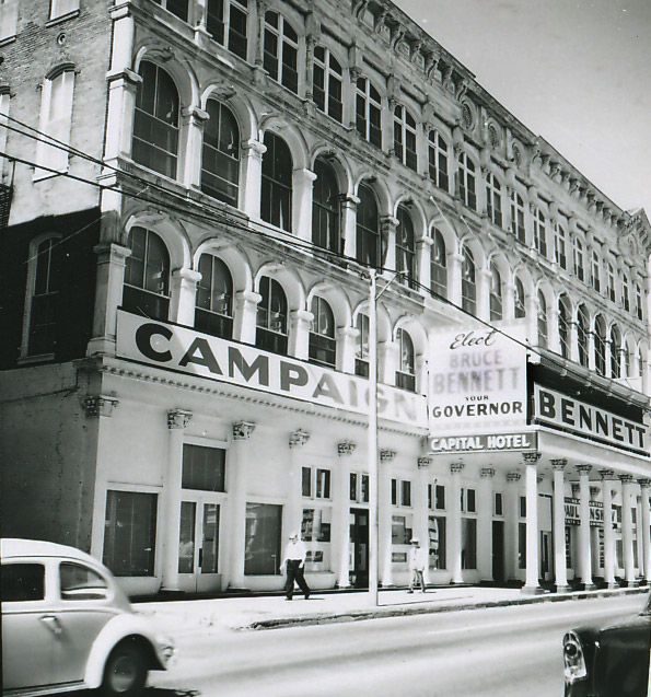Multistory hotel building with arched windows with signs and covered walkway and columns on street
