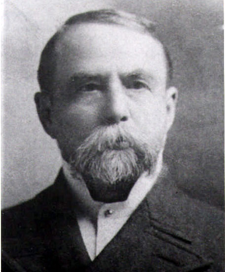 White man with long mustache and short beard in suit