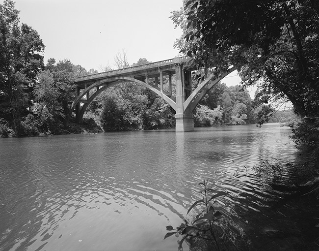 Side view of concrete arch bridge over river taken from shore