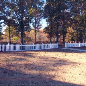 White picket fence and gate on grass with trees behind it