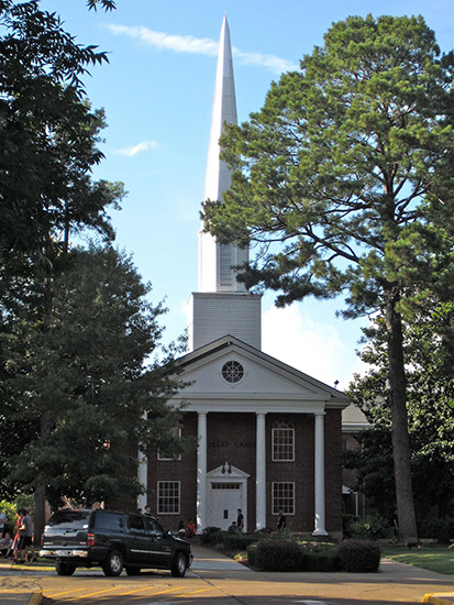 Brick church building with four columns and steeple with vehicle parked in front