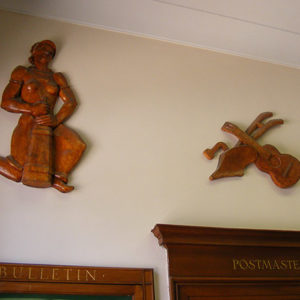 Woodcarvings on wall above labeled wooden frames saying postmaster and bulletin