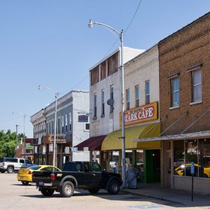 Street with two-story brick storefronts and parked cars