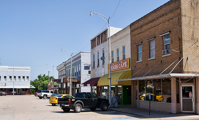 Street with two-story brick storefronts and parked cars