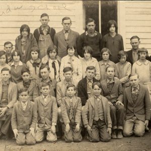 Group of white men women and children posing for group photo outside school building