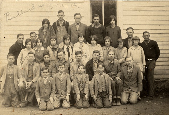 Group of white men women and children posing for group photo outside school building