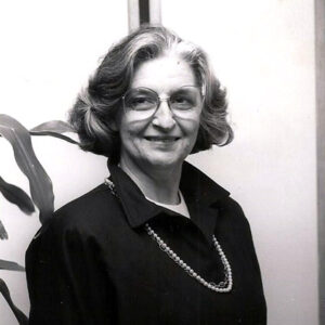 Older woman smiling in collared shirt and pearl necklace with glasses