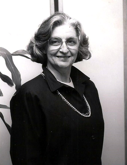 Older woman smiling in collared shirt and pearl necklace with glasses