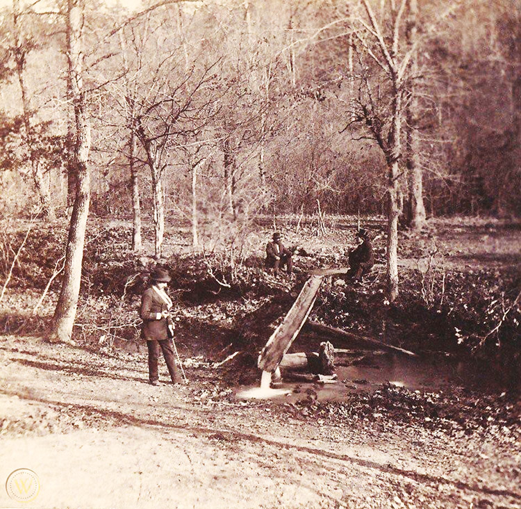 White men in suits and hats using a hollowed out log to reroute natural spring