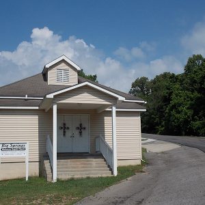 Single-story church building with cupola covered porch and sign next to two-lane road