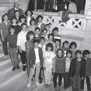 Bald white man with glasses on stone staircase with group of white children