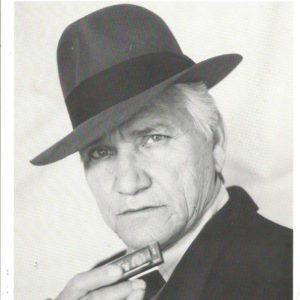 Old white man in hat and suit holding a harmonica
