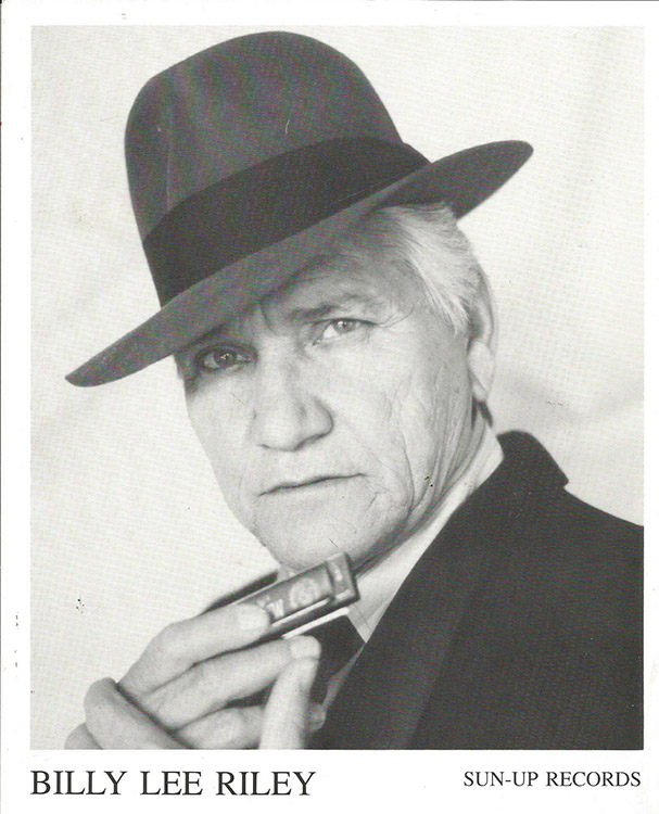 Old white man in hat and suit holding a harmonica