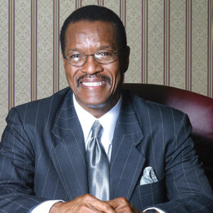 African-American man with mustache and glasses smiling in striped suit and tie