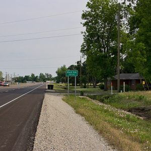 Multilane highway with green "Black Oak" sign on the right near brick house and power lines