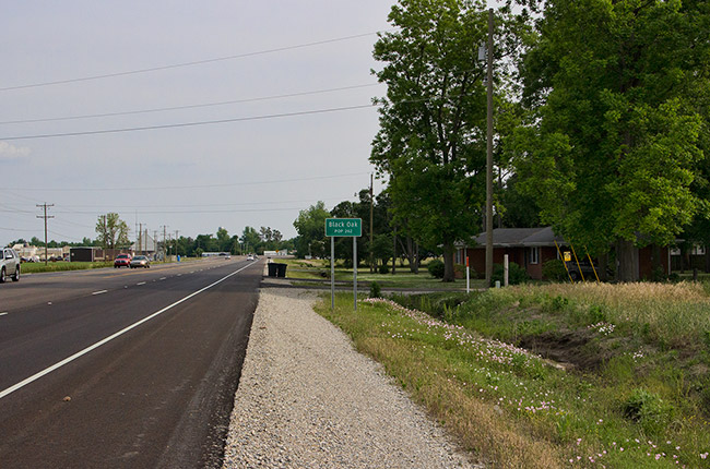 Multilane highway with green "Black Oak" sign on the right near brick house and power lines