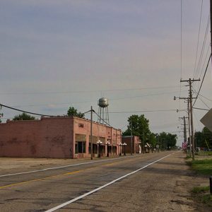 Single-story buildings and houses on two-lane street with water tower in the background