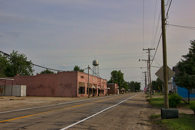Single-story buildings and houses on two-lane street with water tower in the background