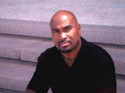 Bald African-American man with close-cropped beard and mustache sitting on steps in black shirt