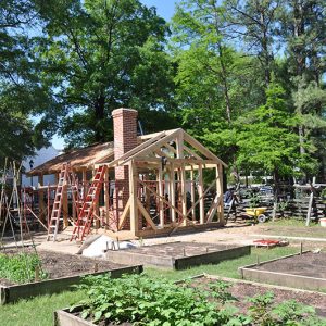 Building under construction with brick chimney with garden plots in the foreground and trees in the background
