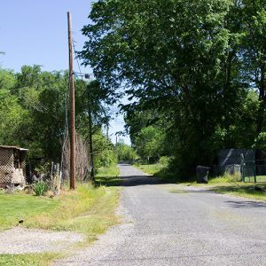 Rural road with house on left side and sheds in yard on the right