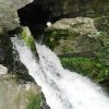 Water rushing out of mountain cave with green moss growing on rock walls