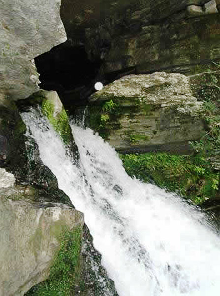 Water rushing out of mountain cave with green moss growing on rock walls