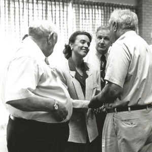 White woman smiling in suit talking to group of older white men