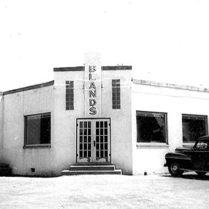 Single-story building with "Blands" written above the doors and cars parked out front
