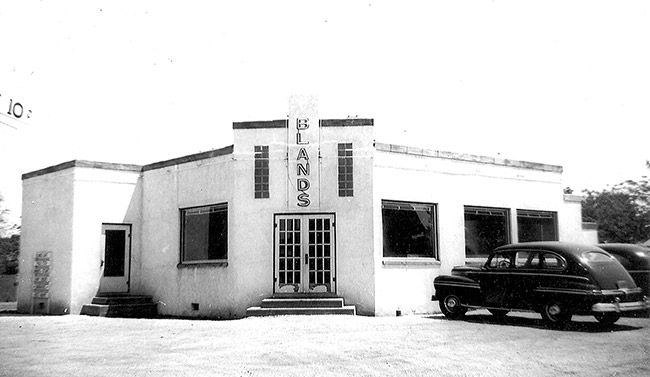 Single-story building with "Blands" written above the doors and cars parked out front