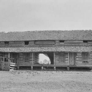 Two-story log cabin with covered porch on dirt