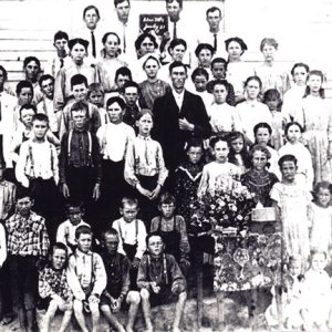 Group of white men women and children posing for photo outside school building