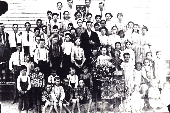 Group of white men women and children posing for photo outside school building