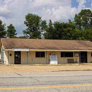 Single-story brick post office building with covered porch and ice cooler on parking lot
