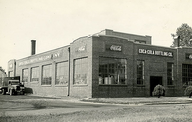 Brick bottling plant building with signs above large windows and truck