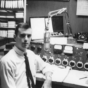 white man sits in radio studio in front of control panel