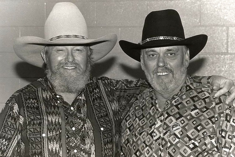 Two white men with beards smiling in colorful shirts and cowboy hats