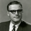 White man with glasses in suit jacket and tie