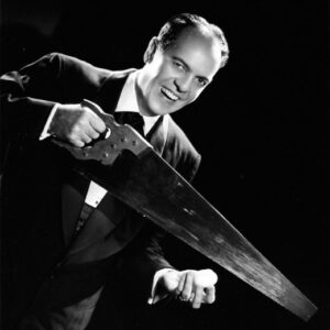 white man in evening dress smiling while holding saw and egg