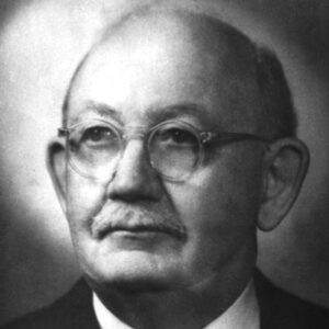 Portrait of balding white man with round glasses mustache wearing suit jacket and tie gazing contemplatively upwards